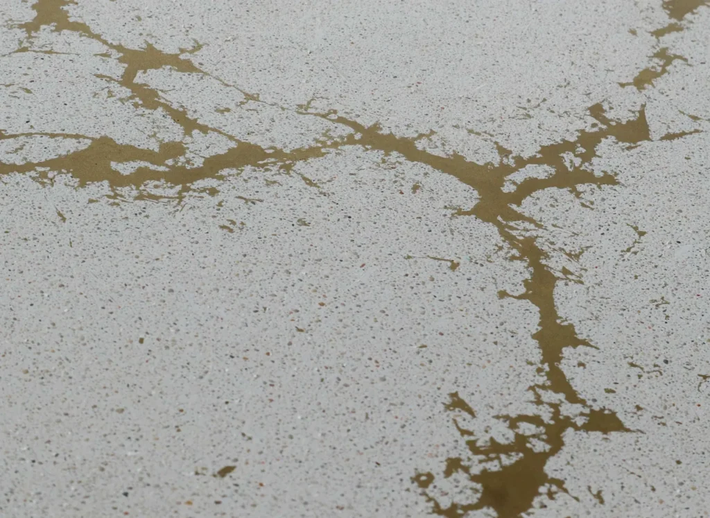Close-up of artisan concrete texture with gold kintsugi-style inlay for modern interior design. Off-white polished concrete with brass metal natural veining inlay for luxury furniture fabrication.