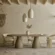 oval-concrete-dining-table-curved-twin-pedestal-Mediterranean-moodern-london-uk Across lifestyle view of the sculptural twin pedestal concrete dining table, styled in a warm Mediterranean vibe minimalist UK interior with textured plaster walls and rustic wooden beams.